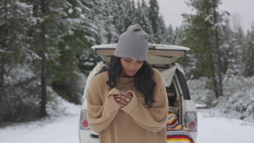 A woman standing in a snow covered area near the back of a vehicle
