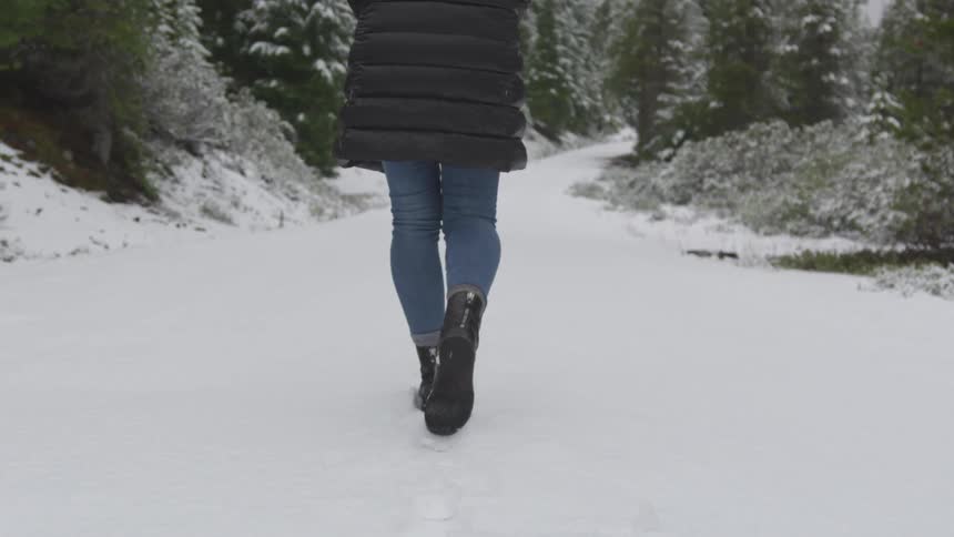 Woman wearing coat walks down on the snowy forest path during daylight