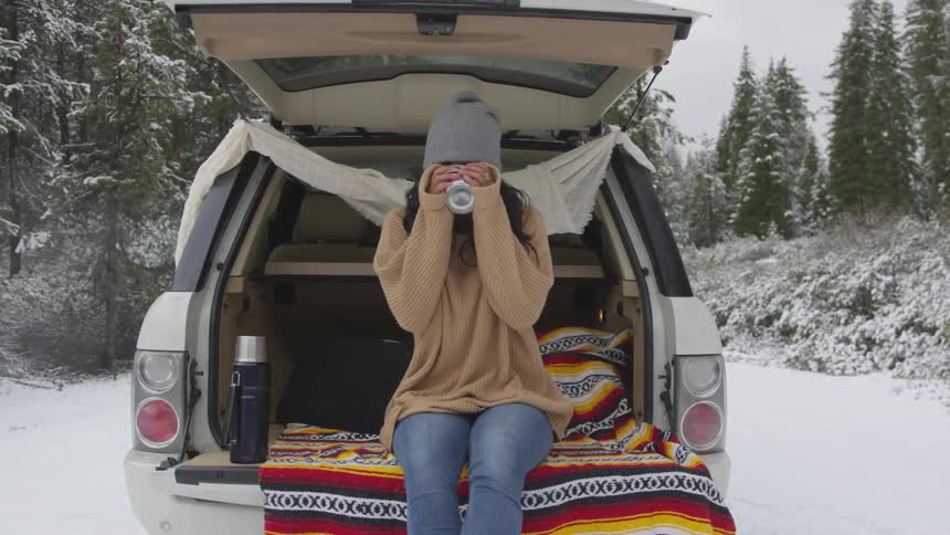 A young girl sits on a tailgate drinking a beverage