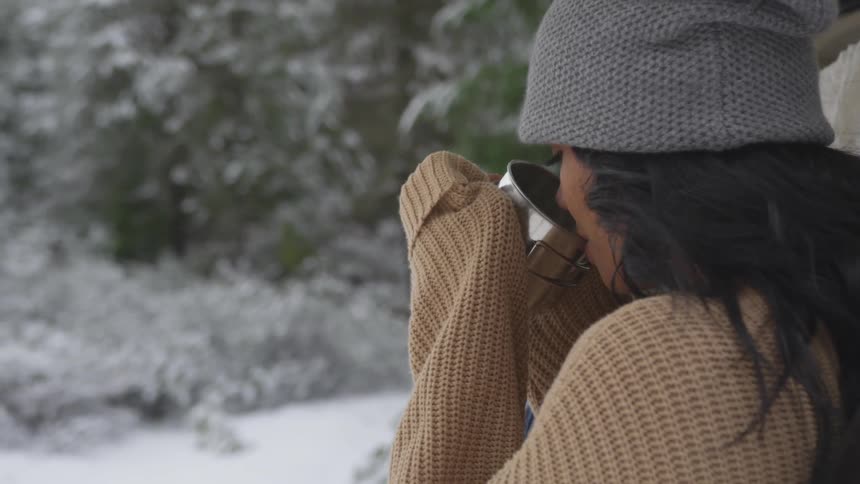 Young woman sips a beverage from the large metal mug on a winter day
