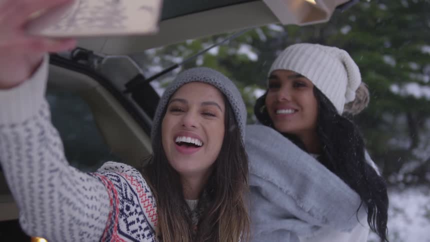 Two women talking a selfie while standing behind a vehicle on a snowy day