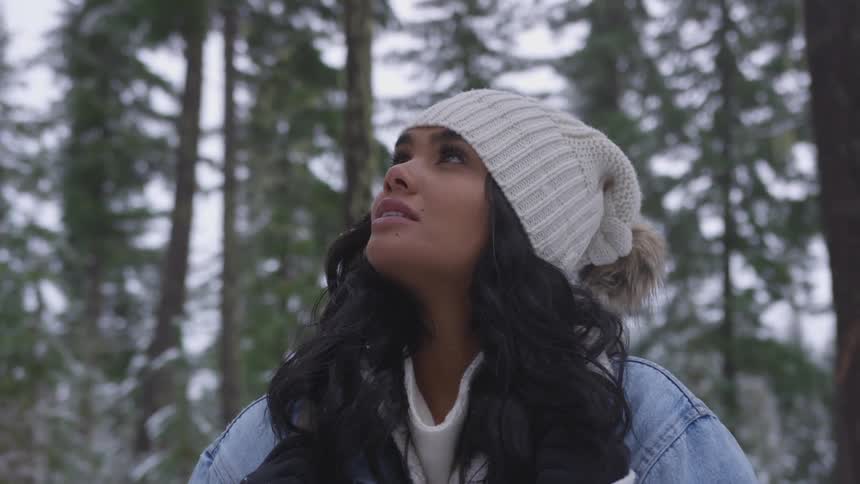 A woman stands in a forest and looks up at the sky