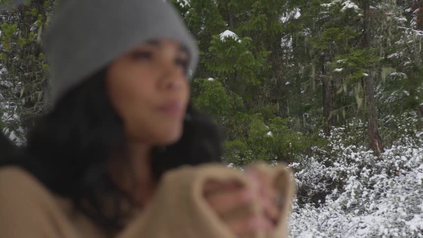 A woman drinks from a cup in a snowy forest
