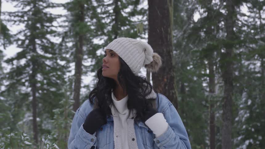 A black woman wearing a coat and a hat walks in the woods