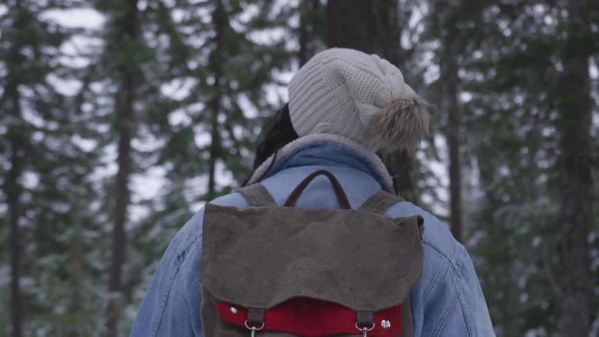 Woman wearing a backpack stands in a forest looking around