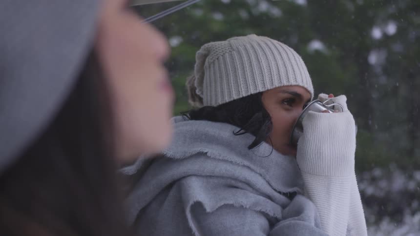 A young woman stands in the snow and drinks out of a mug