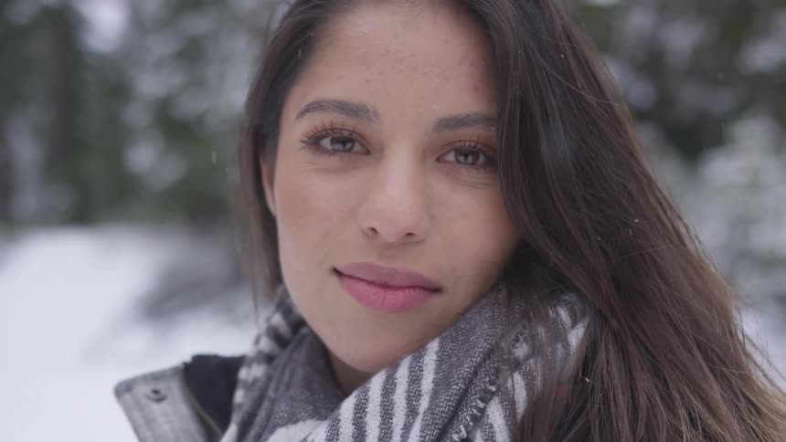 A woman wearing a coat and scarf is standing outside as snow falls