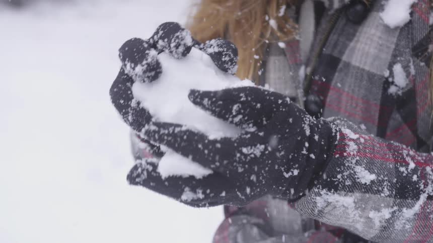 A woman wearing gloves makes a snowball