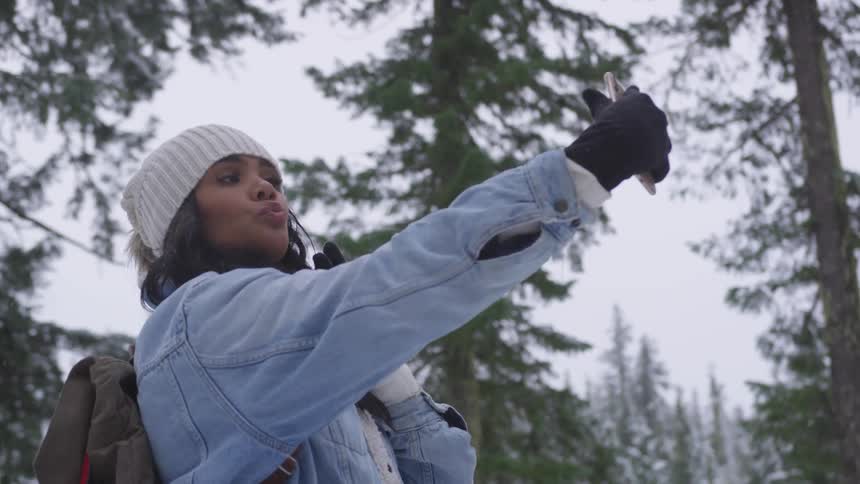 A black woman talking a selfie in a snowy forest