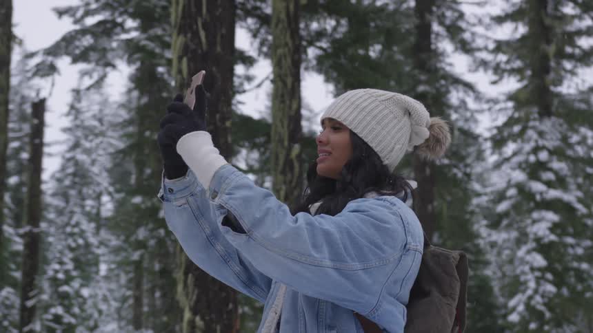 A woman wearing a backpack takes a selfie in the snow covered forest