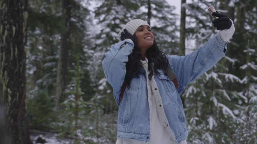 Woman taking selfies with a smartphone on the snow in a forest