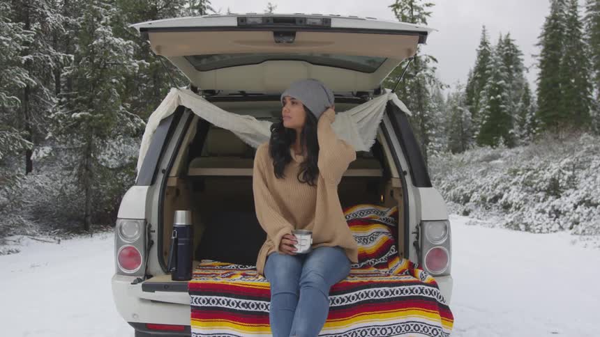 A woman sits in the back of a vehicle parked in the woods