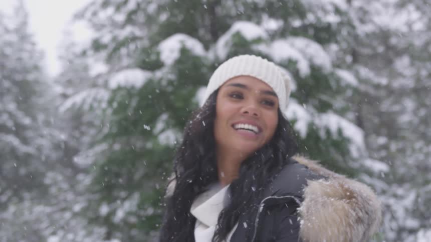Brunette woman picks up snow off the ground and tosses while it snows during daylight