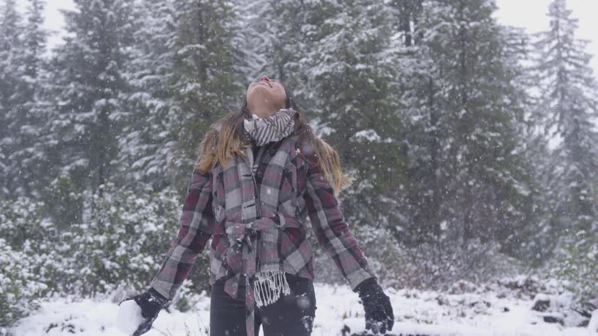 A woman holding a snowball stares into the snow falling from the sky above