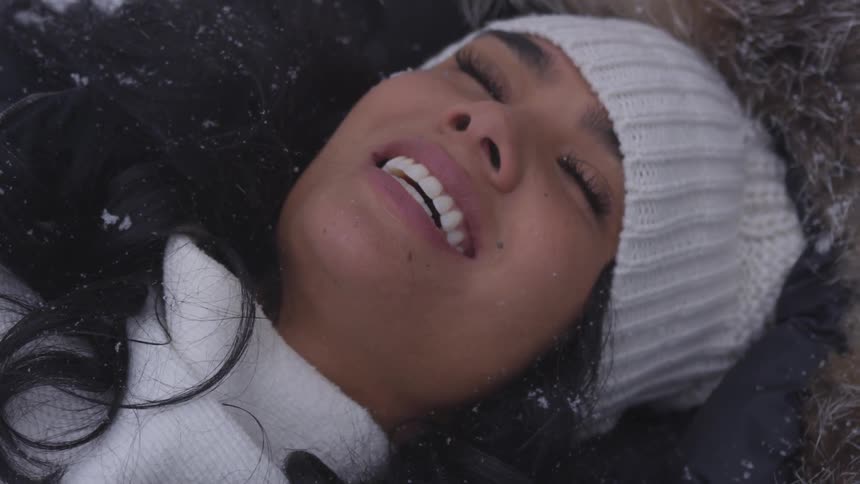 A woman laying on the ground while snow falls on her