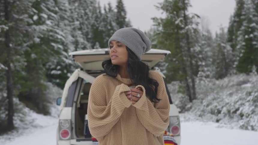 A woman looks around at a snowy landscape with a car in the background