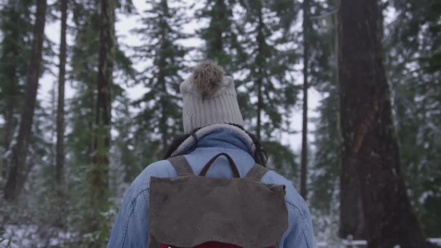 A black woman in winter clothing walks through a snowy forest