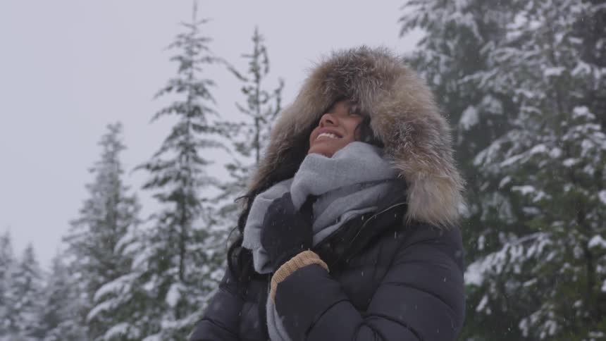 A woman holds her coat tight as she watches the snow fall on her