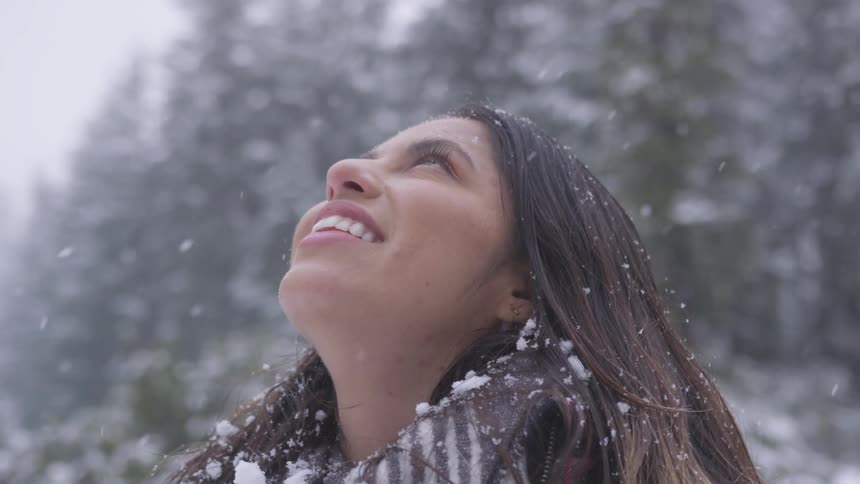 A woman stares into the sky with snow falling around her