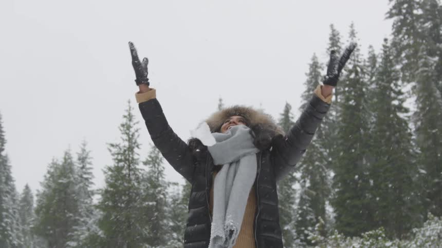A smiling black woman picks up a handful of snow and throw it into the air