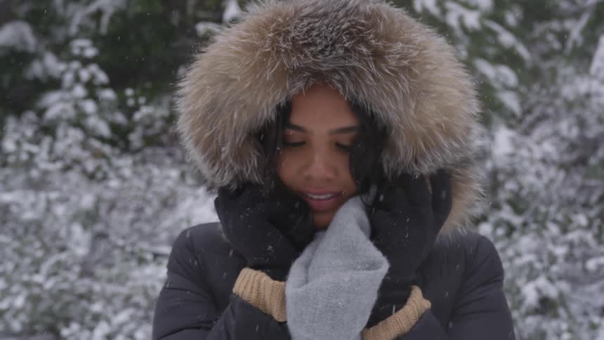 A woman smiles standing outside as it snows