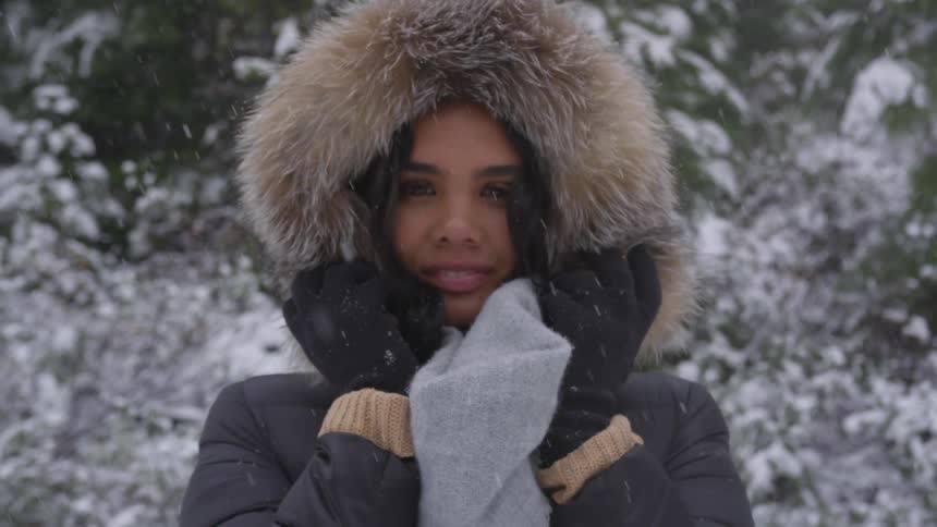 A young woman in a winter coat looks at the camera and smiles