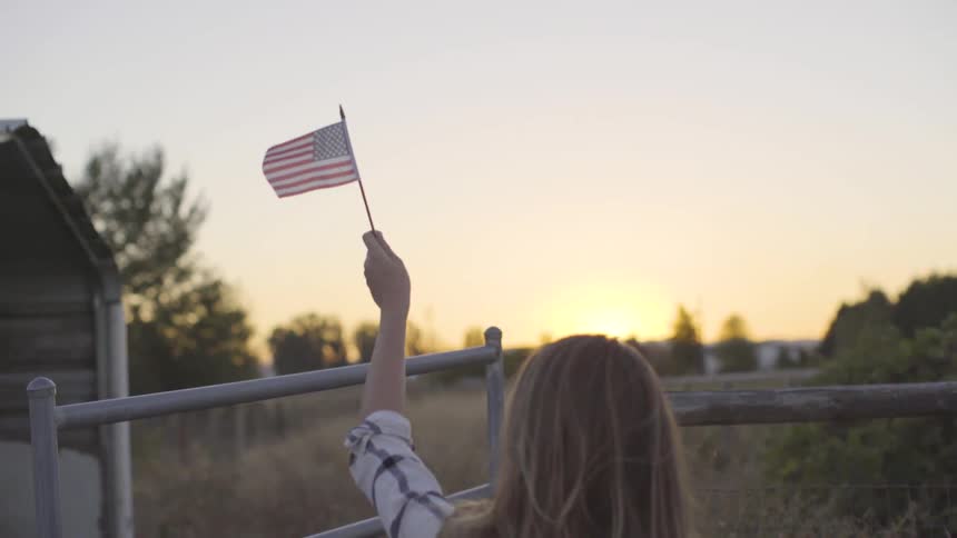 A blonde white woman waves a small american flag outdoors