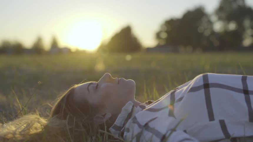 Woman lies on her back in the grass with setting sun behind her