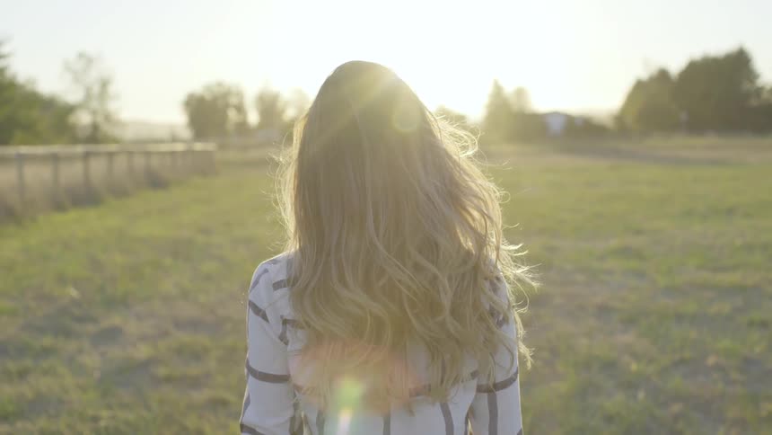 Blonde girl stands in the middle of the farmland while the sun goes down