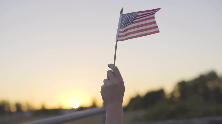 A person is holding a tiny american flag in the wind