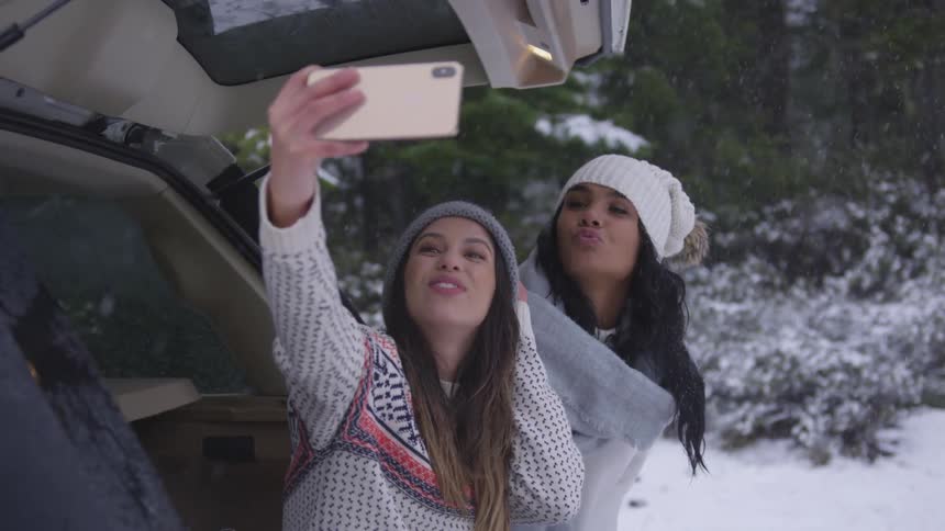 Two women take a selfie by their car as it snows