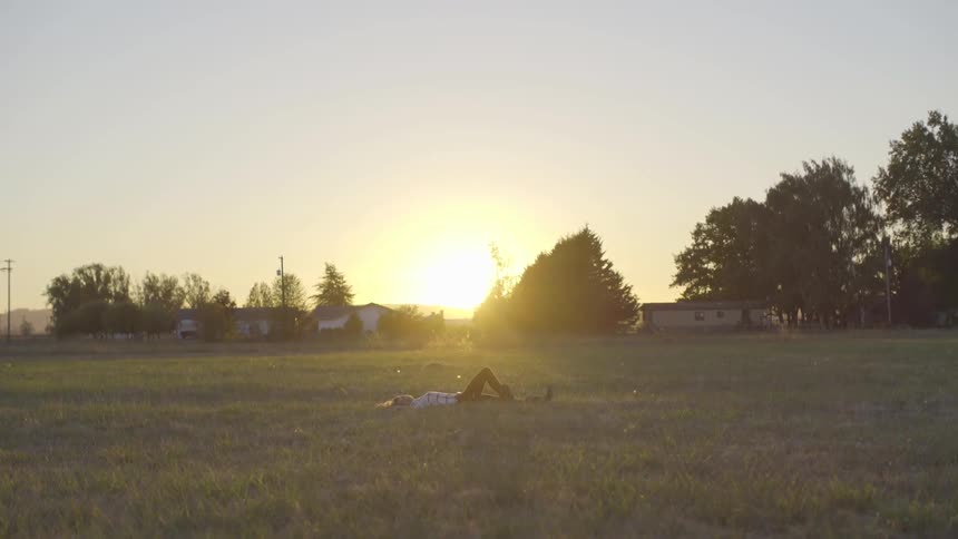 Sun rises as woman lies in field near house