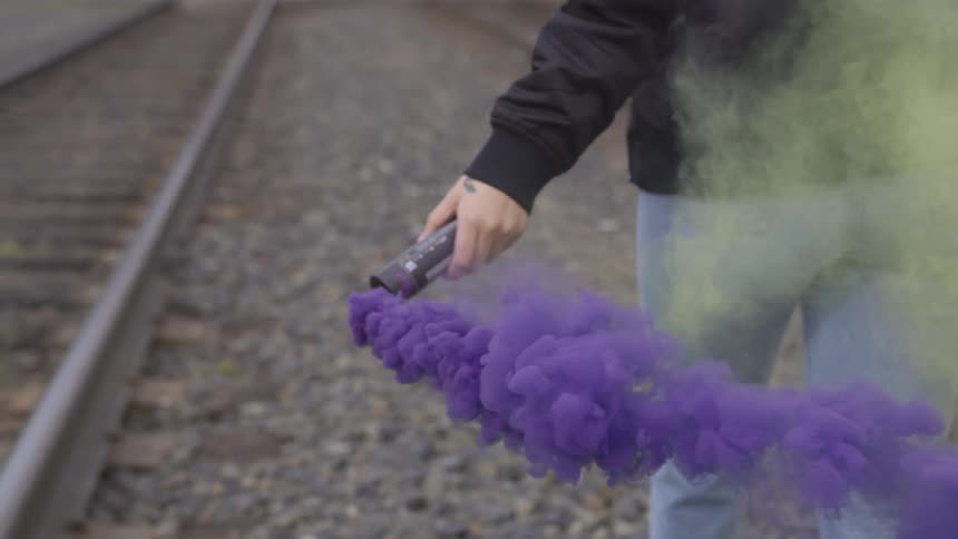 Person spreads colored smoke around between railroad tracks