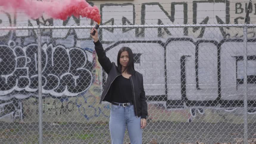 A hispanic woman holds up a smoke grenade