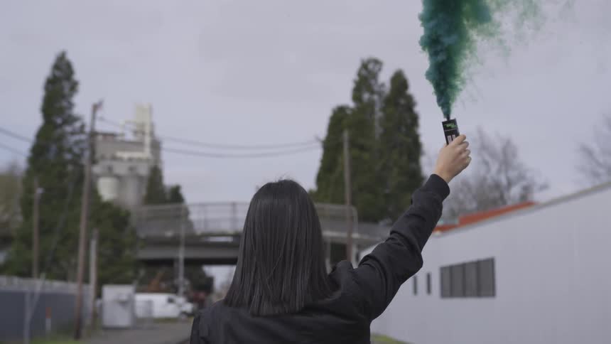 A young woman in a leather jacket holds up a blue flare