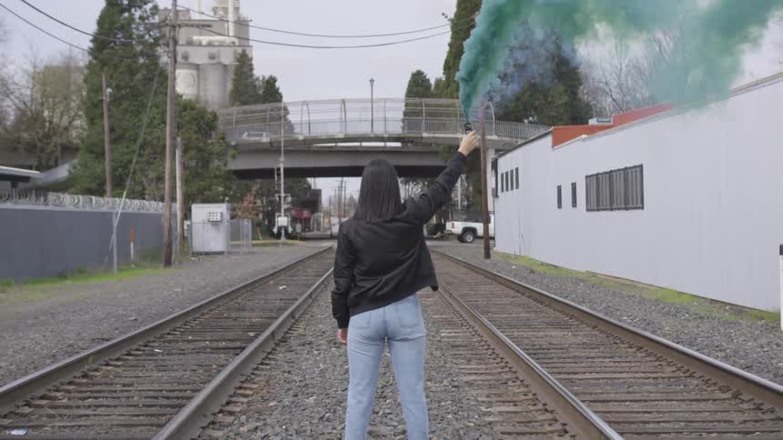A woman standing on railroad tracks with a smoke flare in her hand