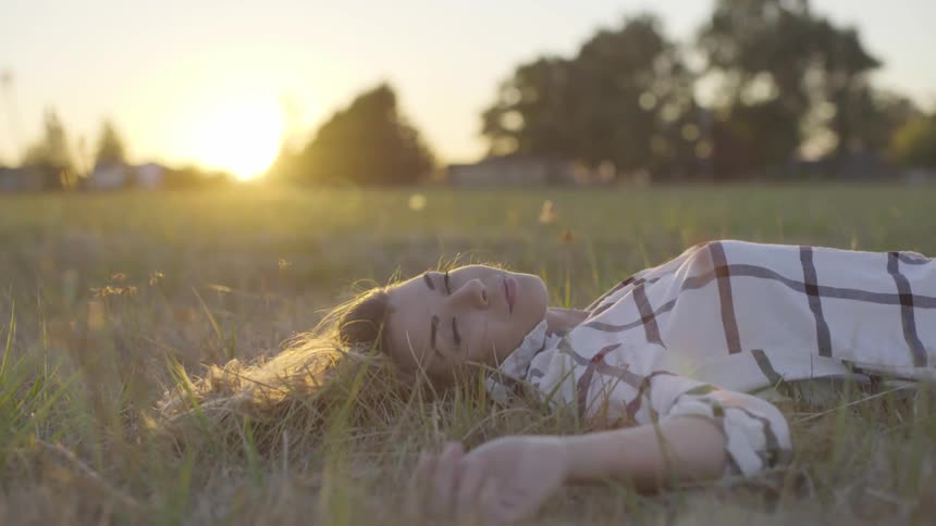 A woman lays in the grass at sunset and turns her head to the left