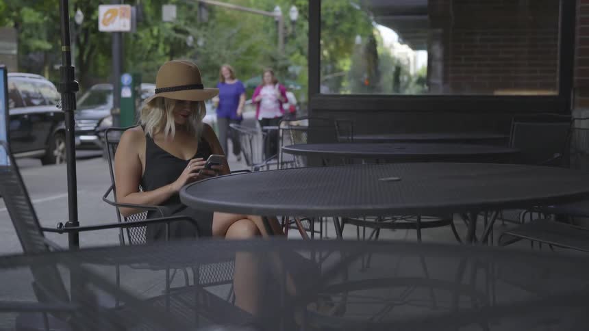 A woman sitting at and outdoor table texting on her phone