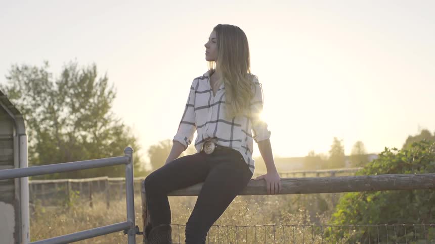 A young woman sits on a fence at sunset