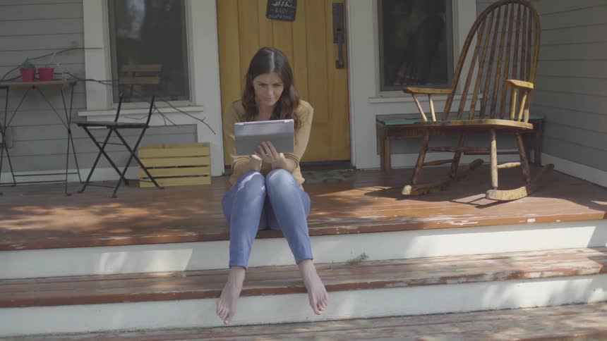 A woman sitting on a porch looking at her tablet