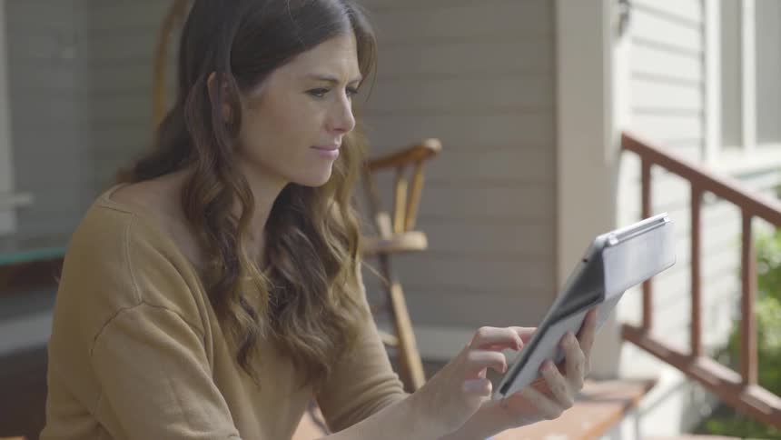 Woman sits on doorstep and uses tablet on a sunny day