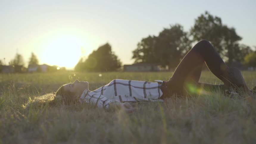 Woman lies down on the grass while the sun goes down