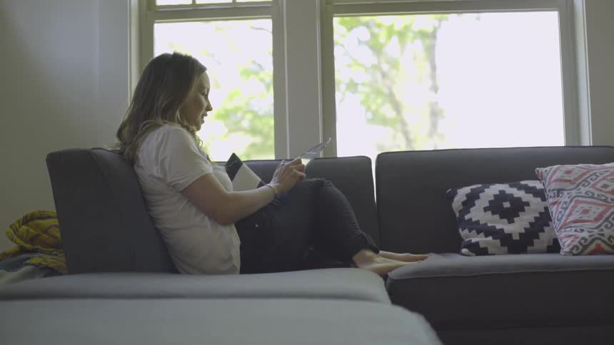 A woman is sitting on the couch using her tablet