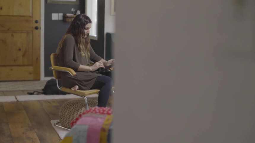 A woman sits in a chair in a living room and uses a tablet computer