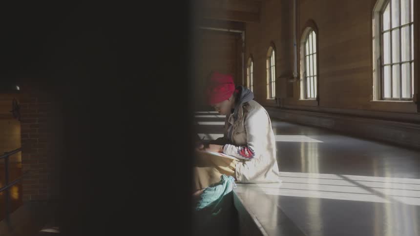 A woman writes on paper while sitting on concrete steps inside a building