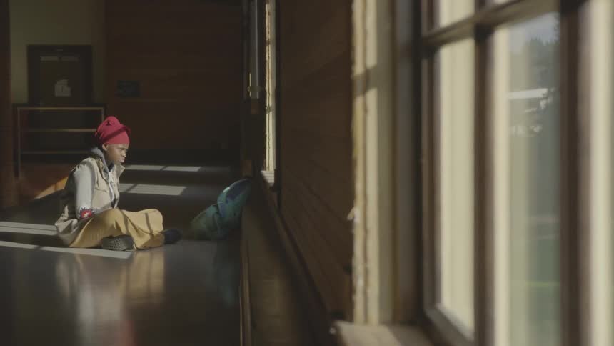 A young woman sits in an empty room looking out the window