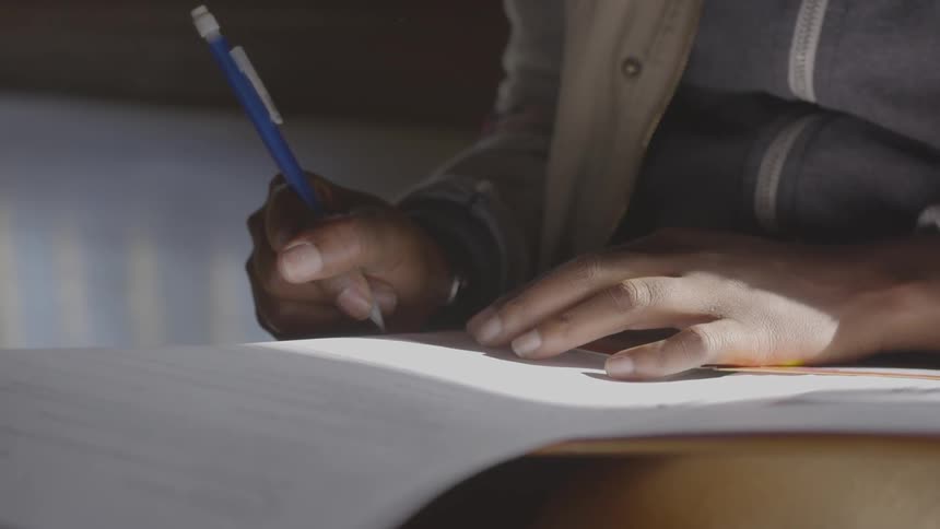 Black person writing on the white paper while sun shines on the hands