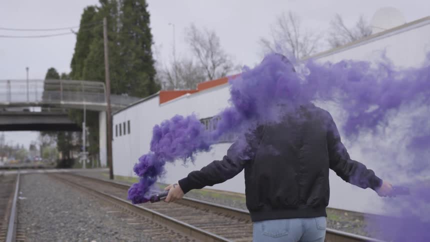 Woman disperses colored smoke as she walks near the train tracks