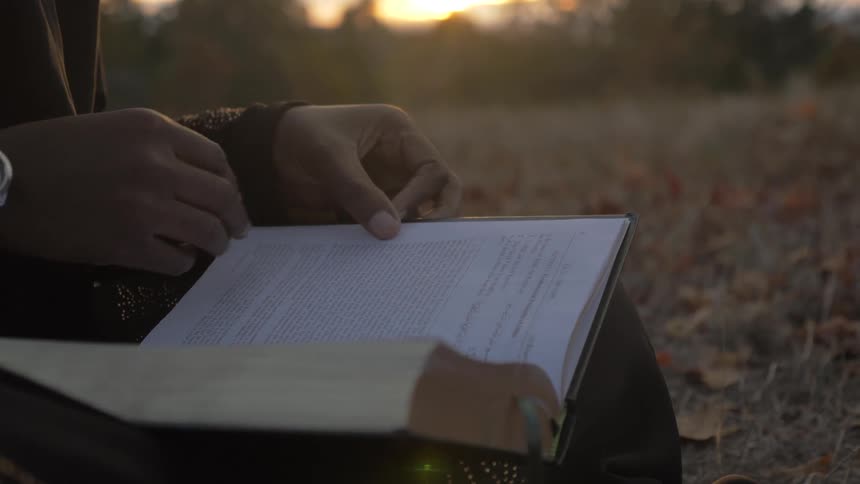 Black person sits down and turns over the page of the book at sunset