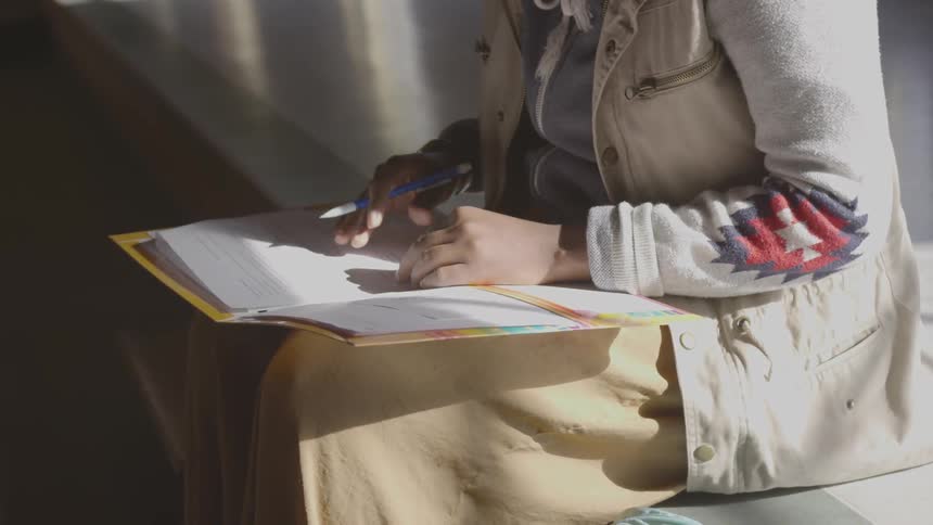 A person writing in a notebook sitting on a step